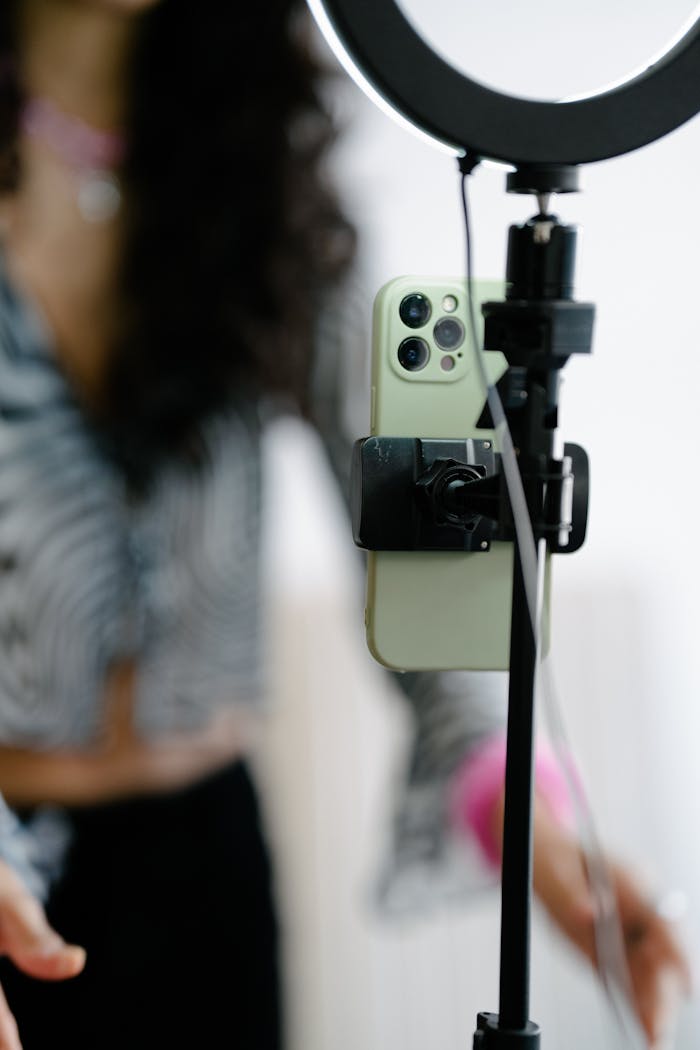 about-img A woman using a smartphone and ring light setup for content creation.