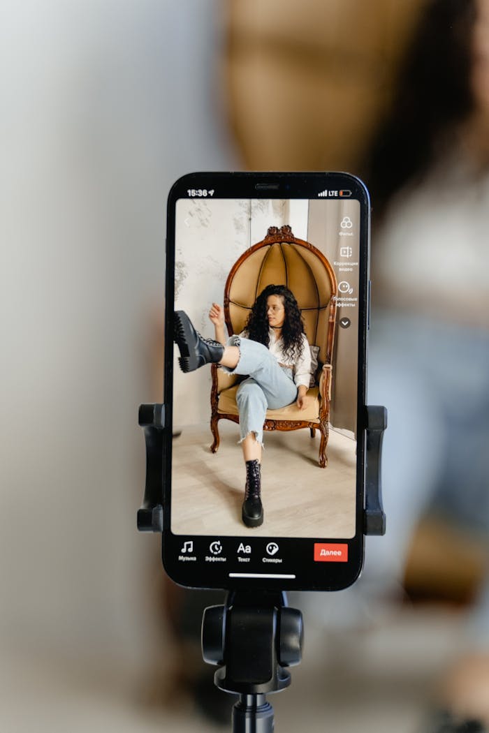 Woman sitting on a chair being filmed on a smartphone with a blurred background.
