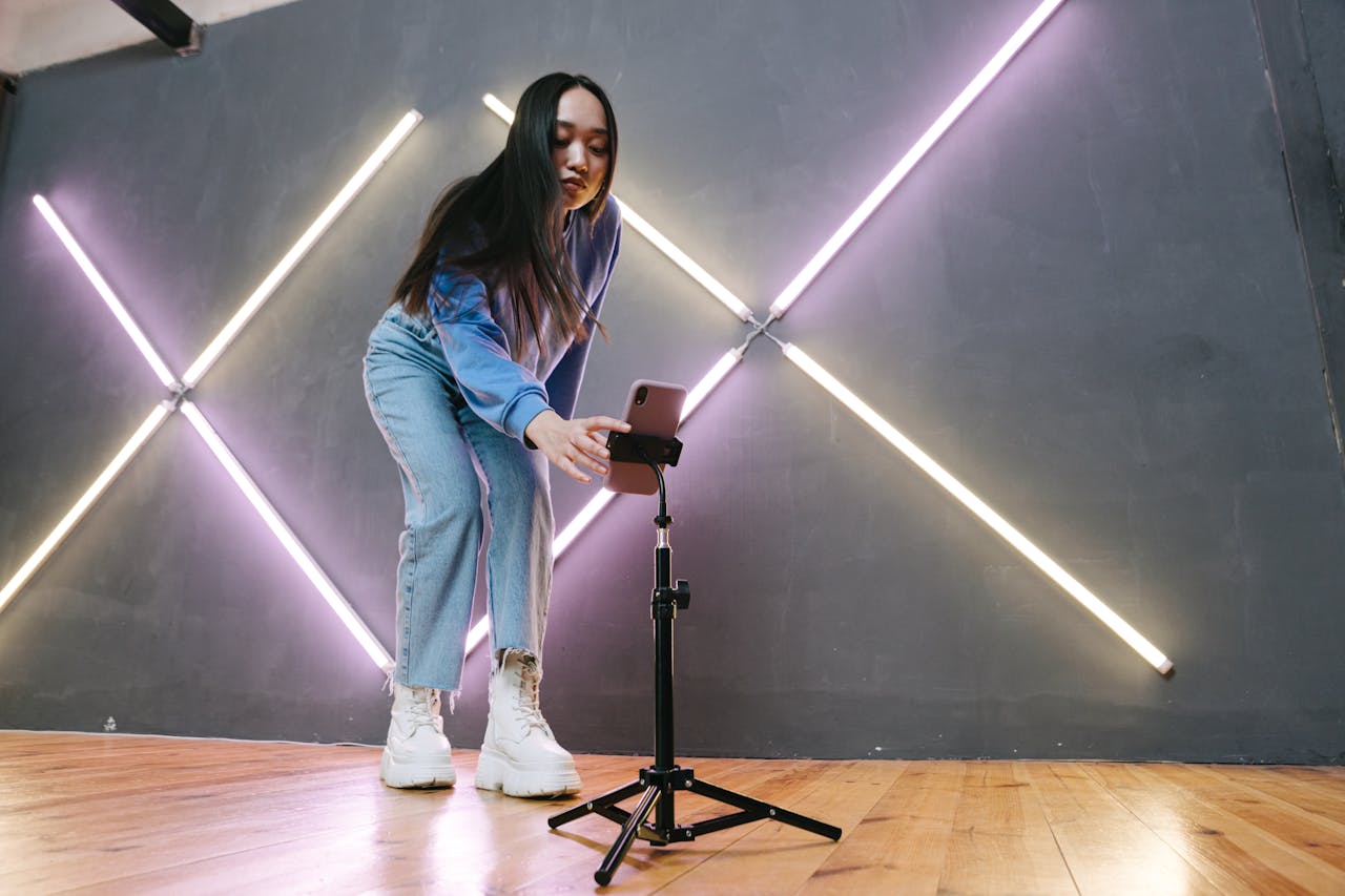 Young Asian woman setting up smartphone for streaming indoors with neon lights.
